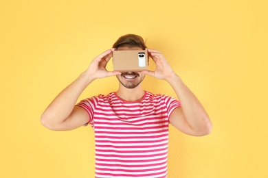 Young man using cardboard virtual reality headset on color background