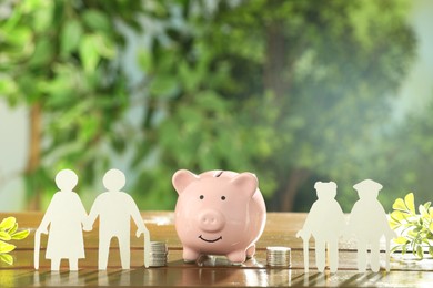 Pension savings. Figures of elderly people, stacked coins, piggy bank and green twigs on wooden table outdoors