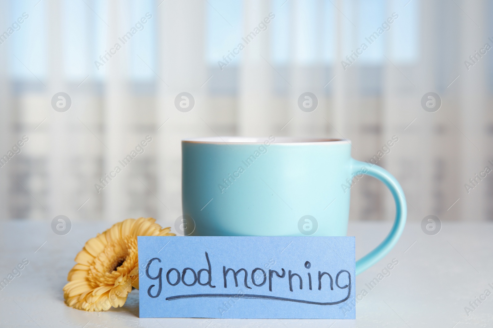 Photo of Delicious coffee, beautiful flower and card with words GOOD MORNING on white table indoors