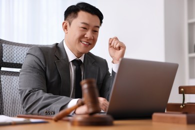 Happy notary working with laptop at wooden table in office