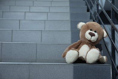 Lonely teddy bear on staircase near metal railing indoors, space for text