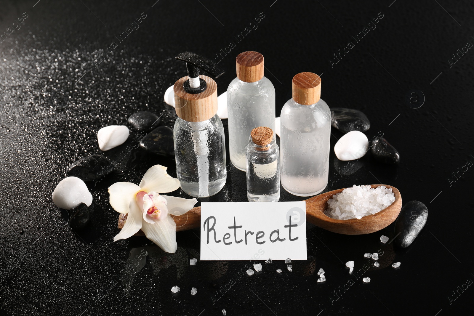 Photo of Card with word Retreat, different spa products and orchid flower on wet black table