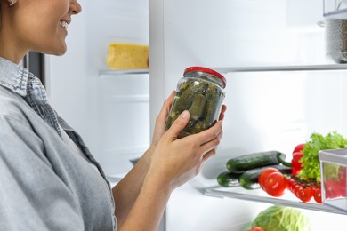 Young woman taking jar of pickles out of refrigerator, closeup