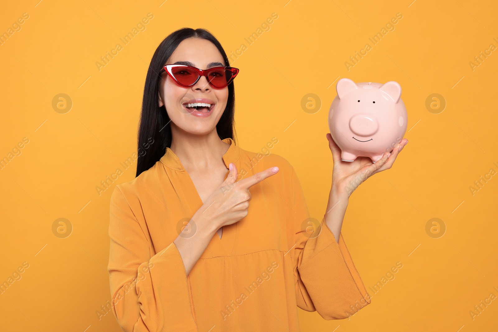 Photo of Emotional young woman with piggy bank on orange background