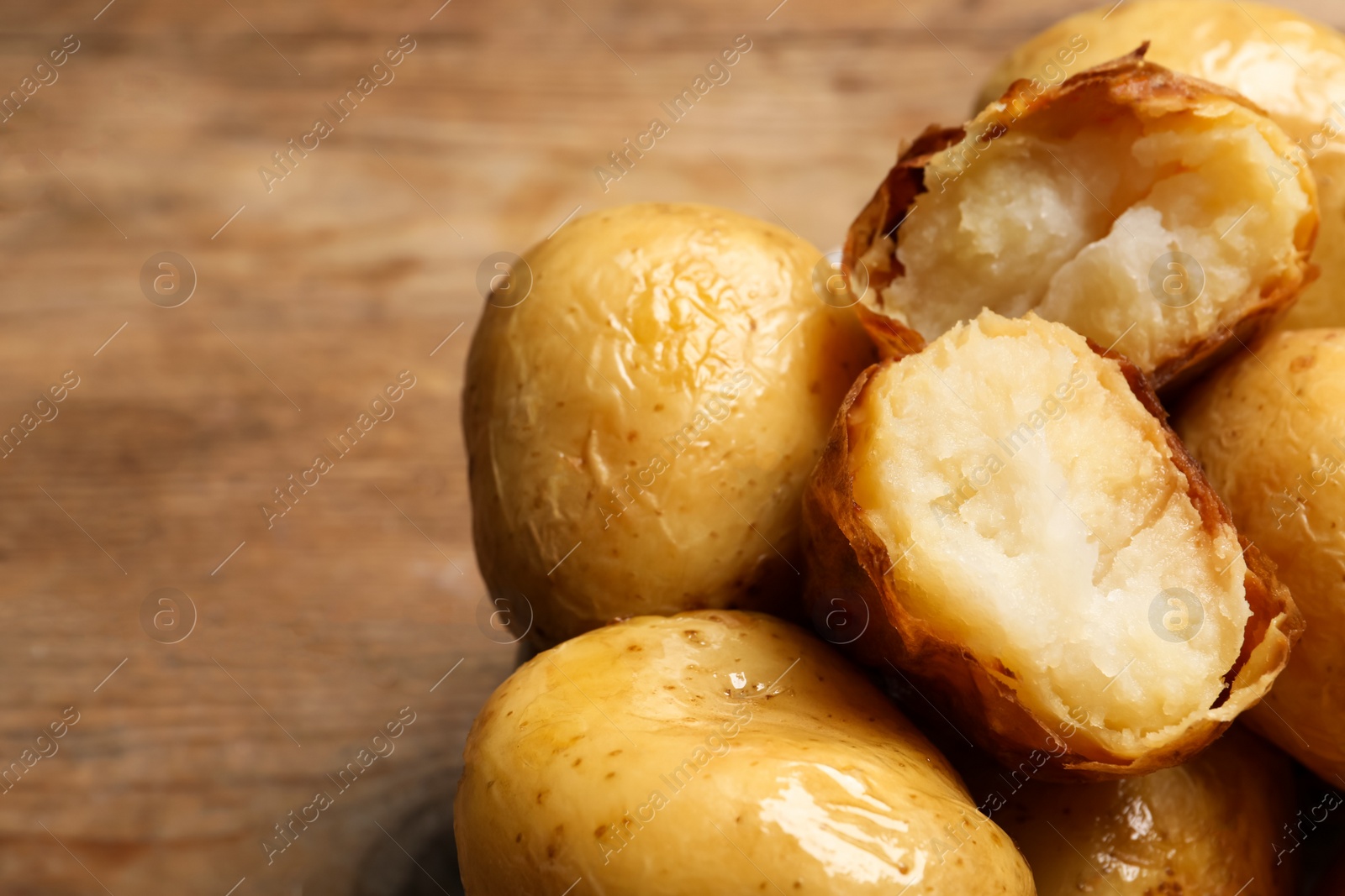 Photo of Bowl of tasty whole baked potatoes on wooden table, closeup. Space for text