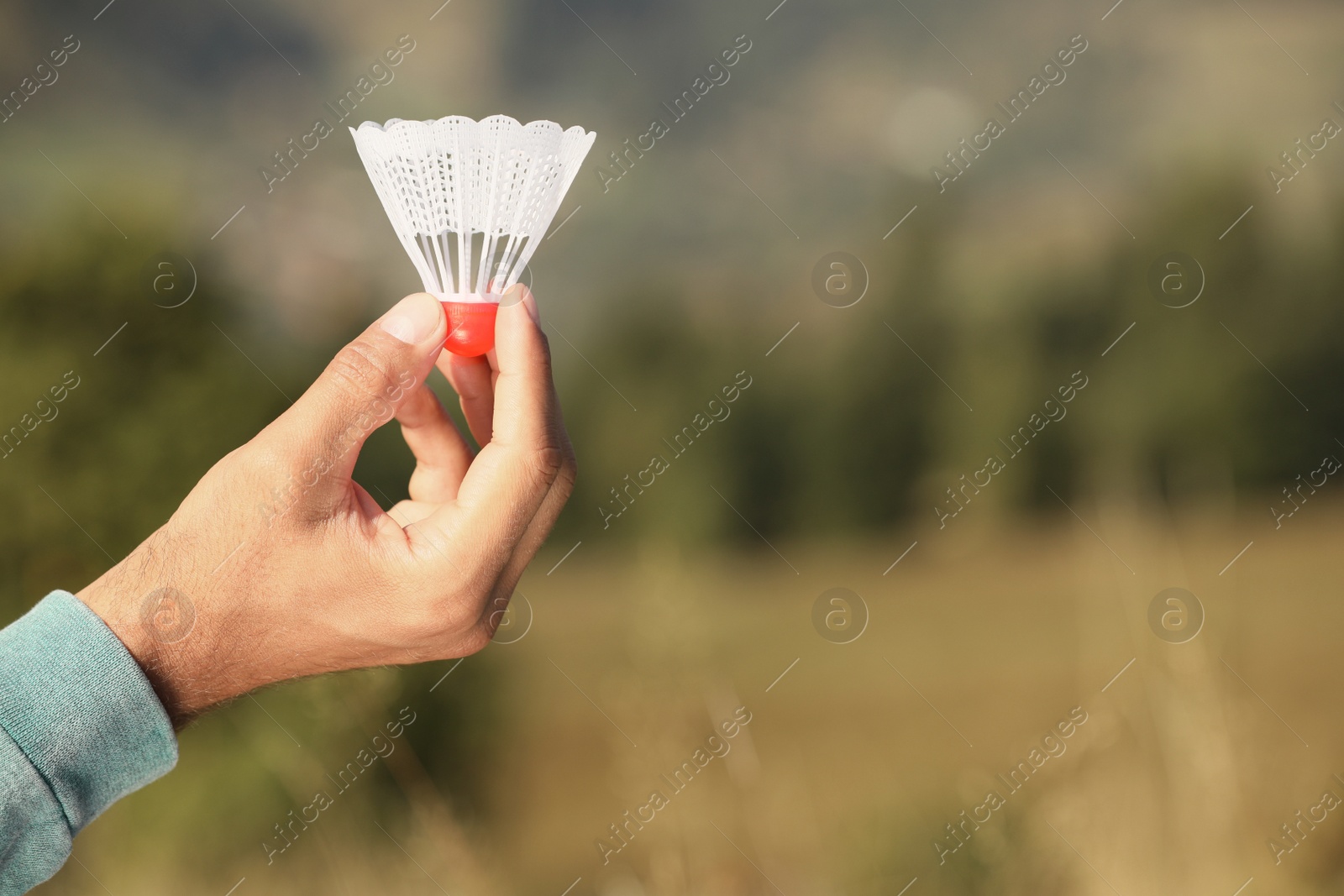 Photo of Man holding badminton shuttlecock on blurred background, closeup. Space for text