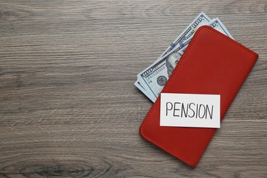 Photo of Card with word Pension, wallet and dollar banknotes on wooden table, flat lay. Space for text