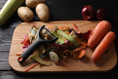 Photo of Peels of fresh vegetables and peeler on dark wooden table, closeup