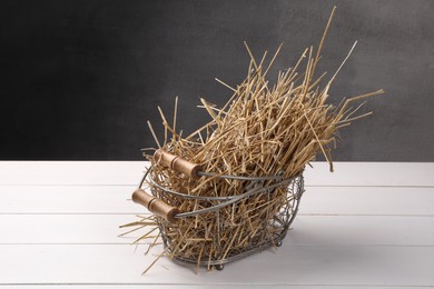 Photo of Dried straw in metal basket on white wooden table