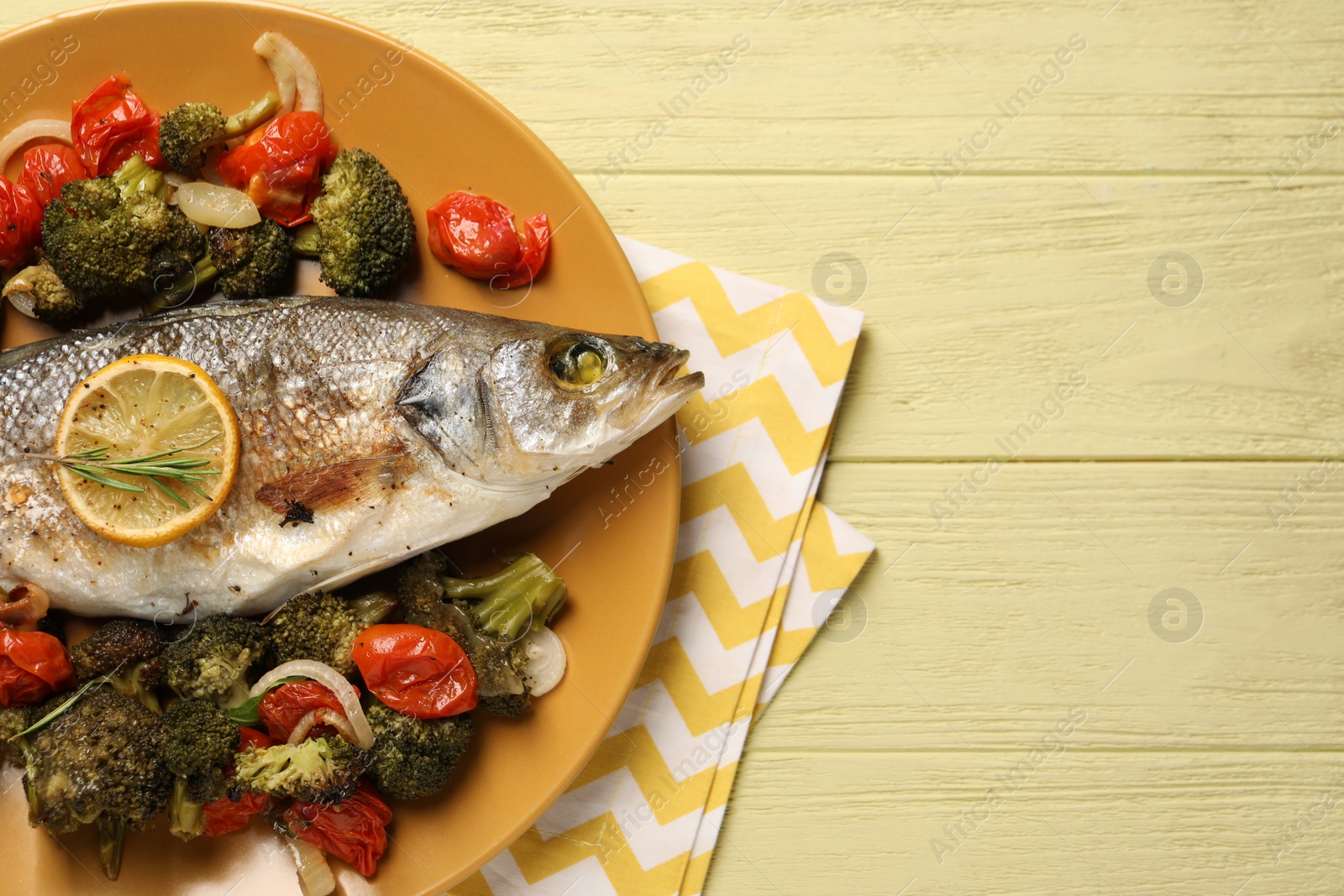 Photo of Delicious baked fish and vegetables on yellow wooden table, top view. Space for text