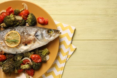 Photo of Delicious baked fish and vegetables on yellow wooden table, top view. Space for text