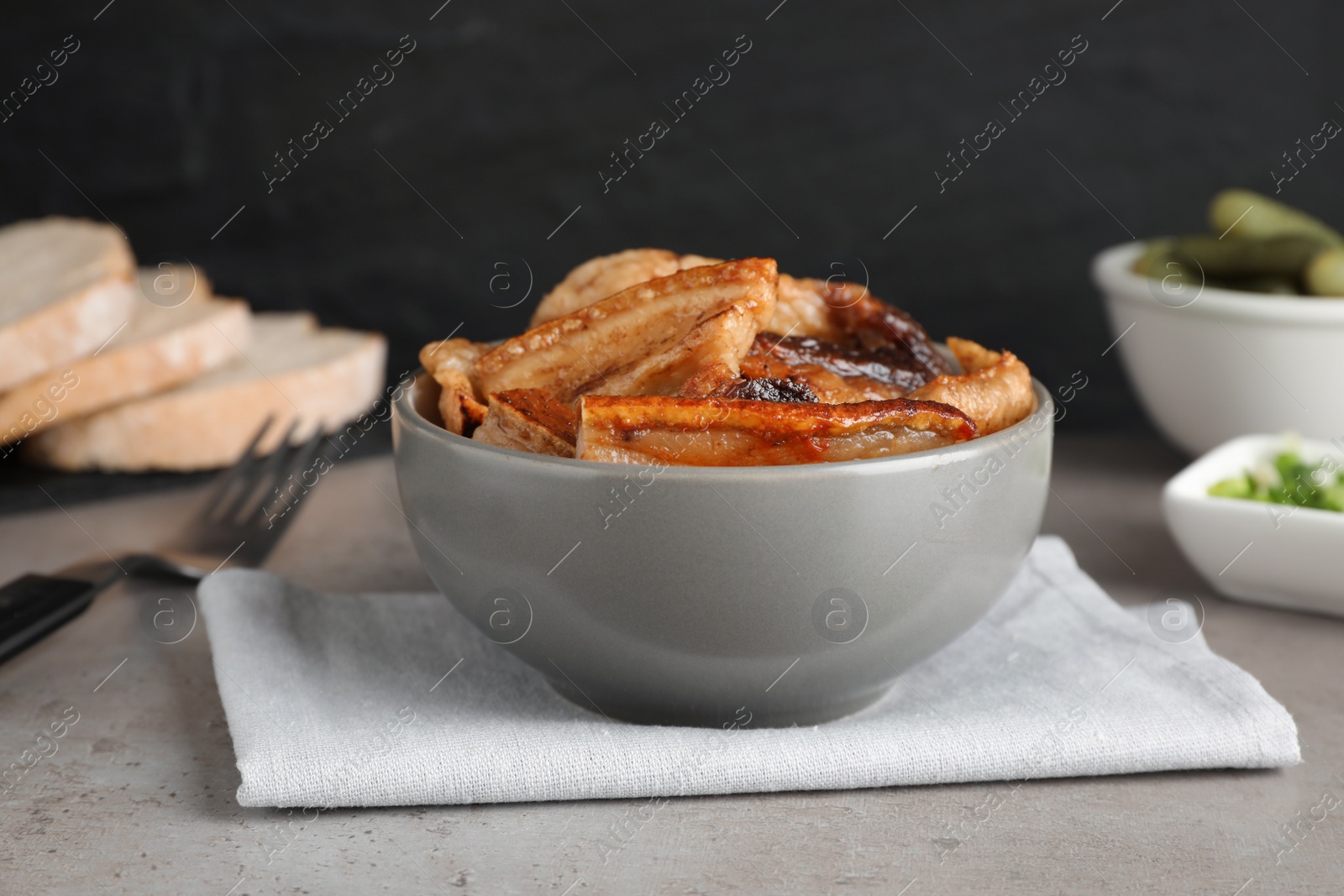 Photo of Bowl with tasty fried pork fatback slices on grey table