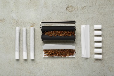 Photo of Roller with tobacco, filters and hand rolled cigarettes on light grey table, flat lay