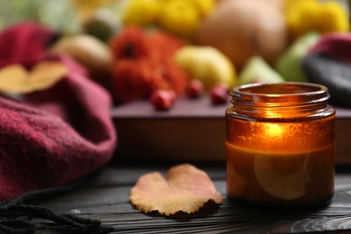 Photo of Burning scented candle and book on wooden table, space for text. Autumn season