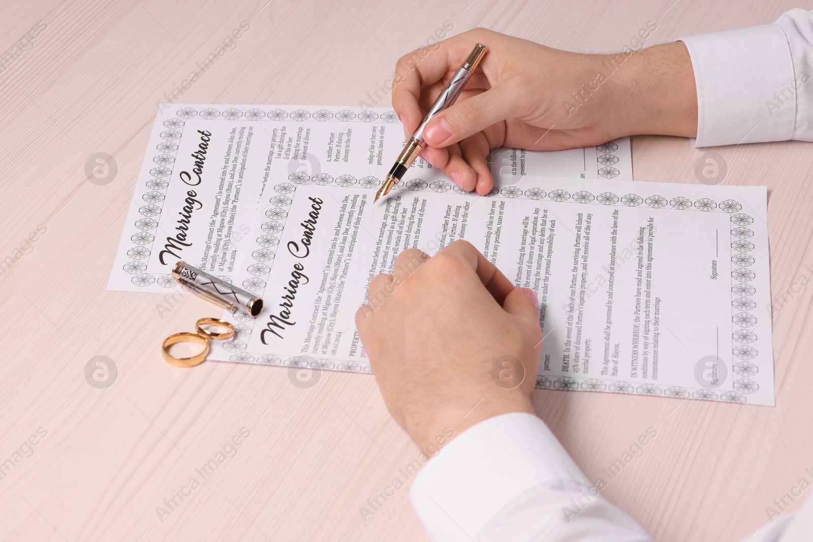 Photo of Man signing marriage contract at light wooden table, closeup