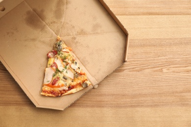 Photo of Cardboard box with pizza piece on wooden background, top view with space for text