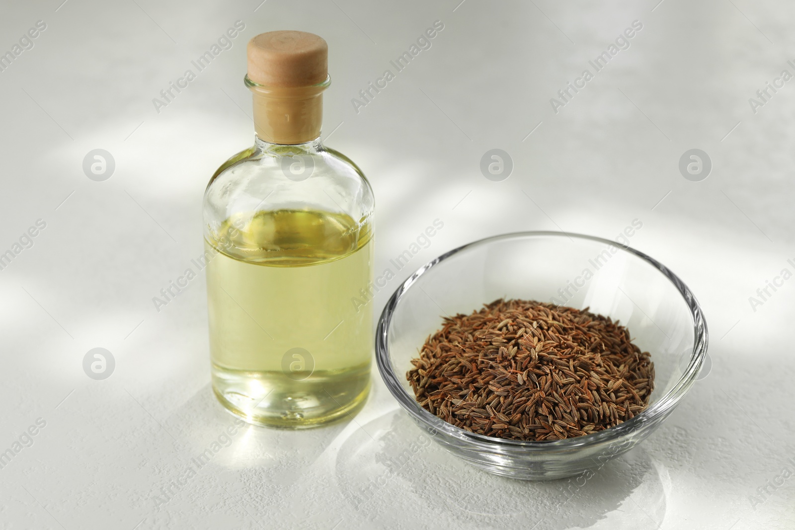 Photo of Caraway (Persian cumin) seeds in bowl and essential oil on white table