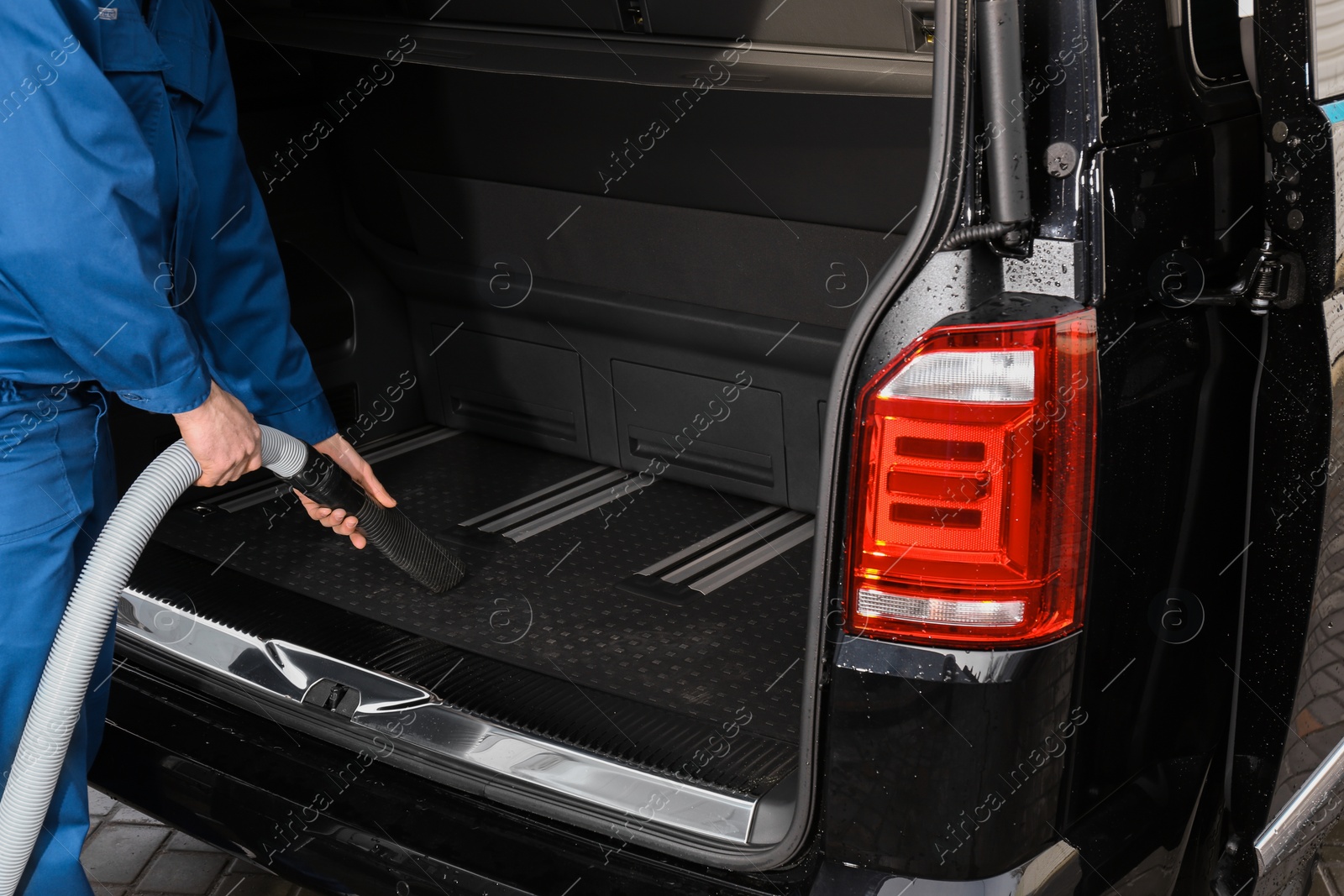 Photo of Worker using vacuum cleaner in automobile trunk at car wash, closeup