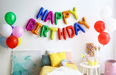 Photo of Phrase HAPPY BIRTHDAY made of colorful balloon letters and table with treats in modern bedroom