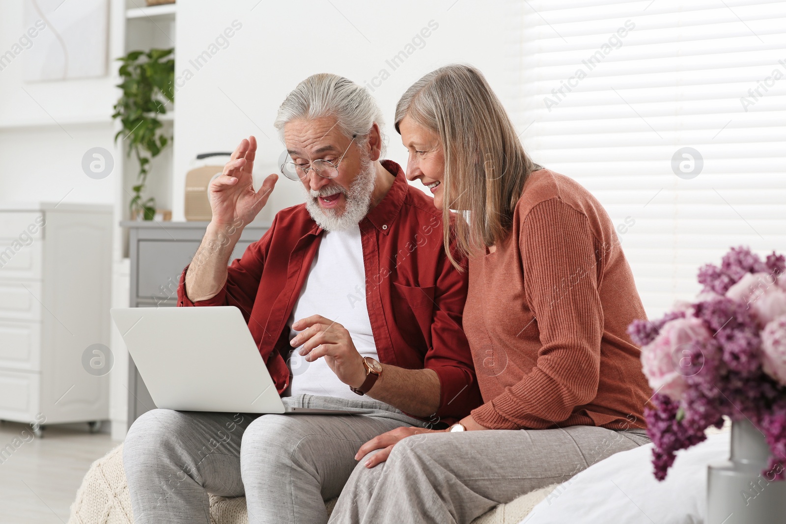 Photo of Senior couple using laptop on sofa at home