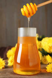 Jar with organic honey and chrysanthemum flowers on wooden table