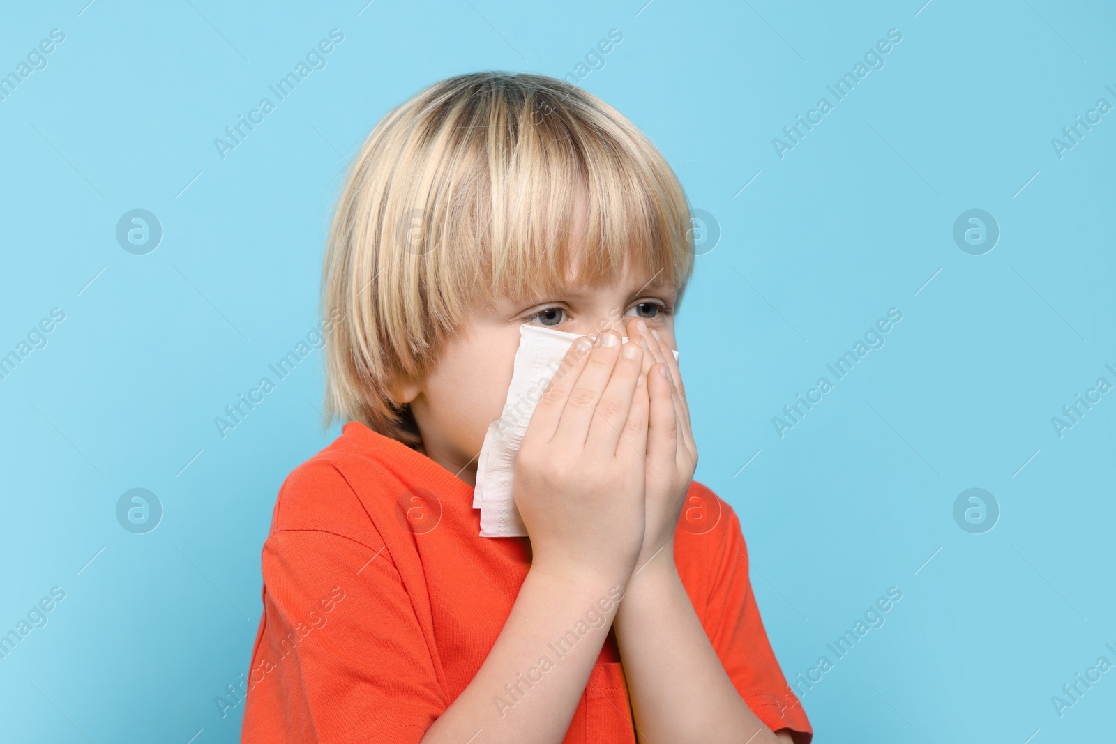 Photo of Boy blowing nose in tissue on light blue background. Cold symptoms