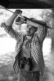 Photo of Young man with binoculars near van outdoors, black and white effect. Camping season