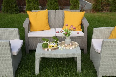 Photo of Easter decorations. Bouquet of tulips in vase, bunny figures and decorated eggs on table in backyard