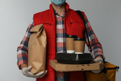 Photo of Courier in protective gloves holding order on light background, closeup. Food delivery service during coronavirus quarantine