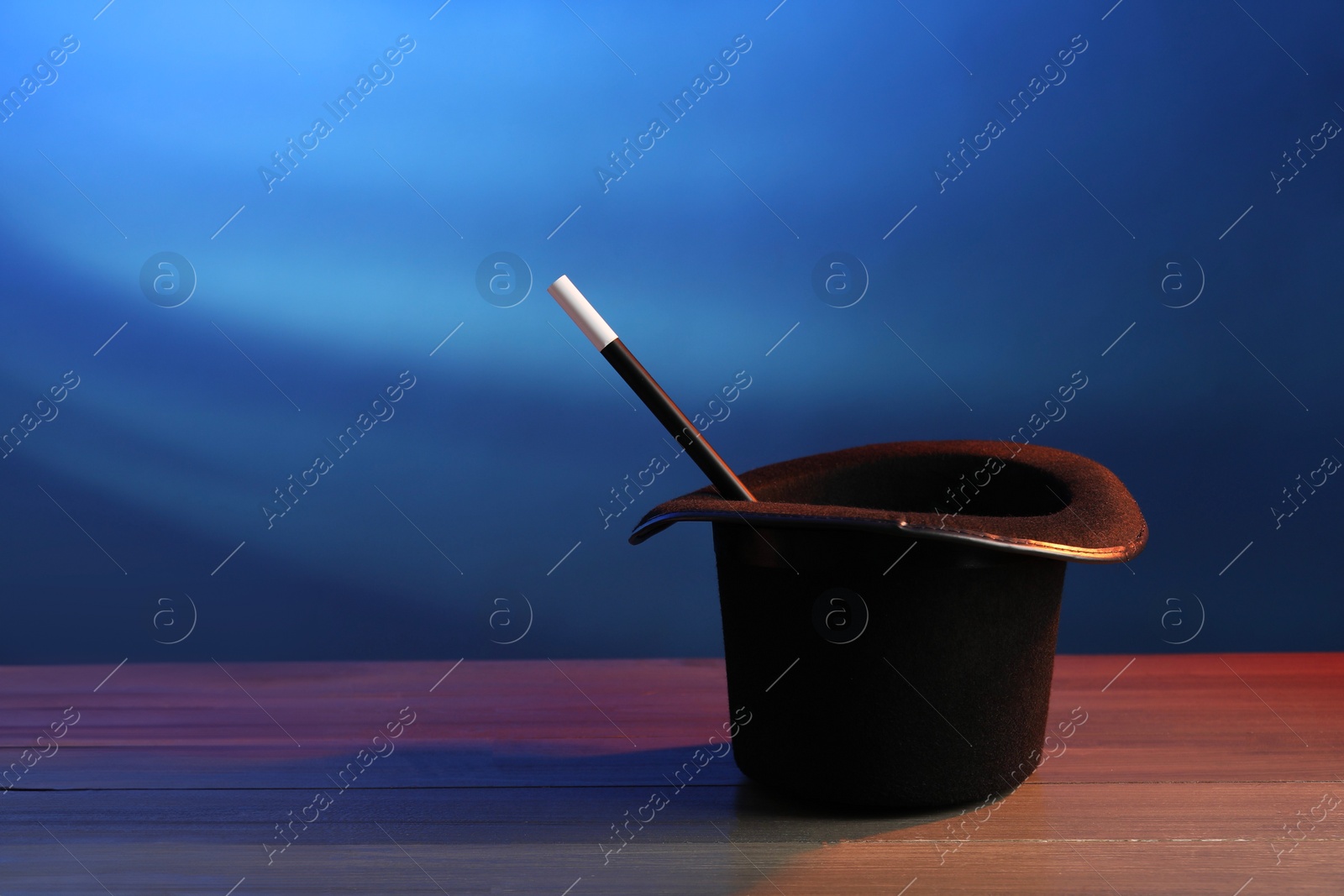 Photo of Magician's hat and wand on wooden table against blue background, space for text