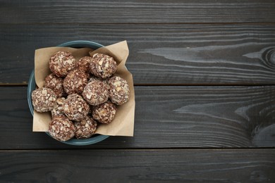 Photo of Bowl of delicious sweet chocolate candies on dark wooden table, top view. Space for text