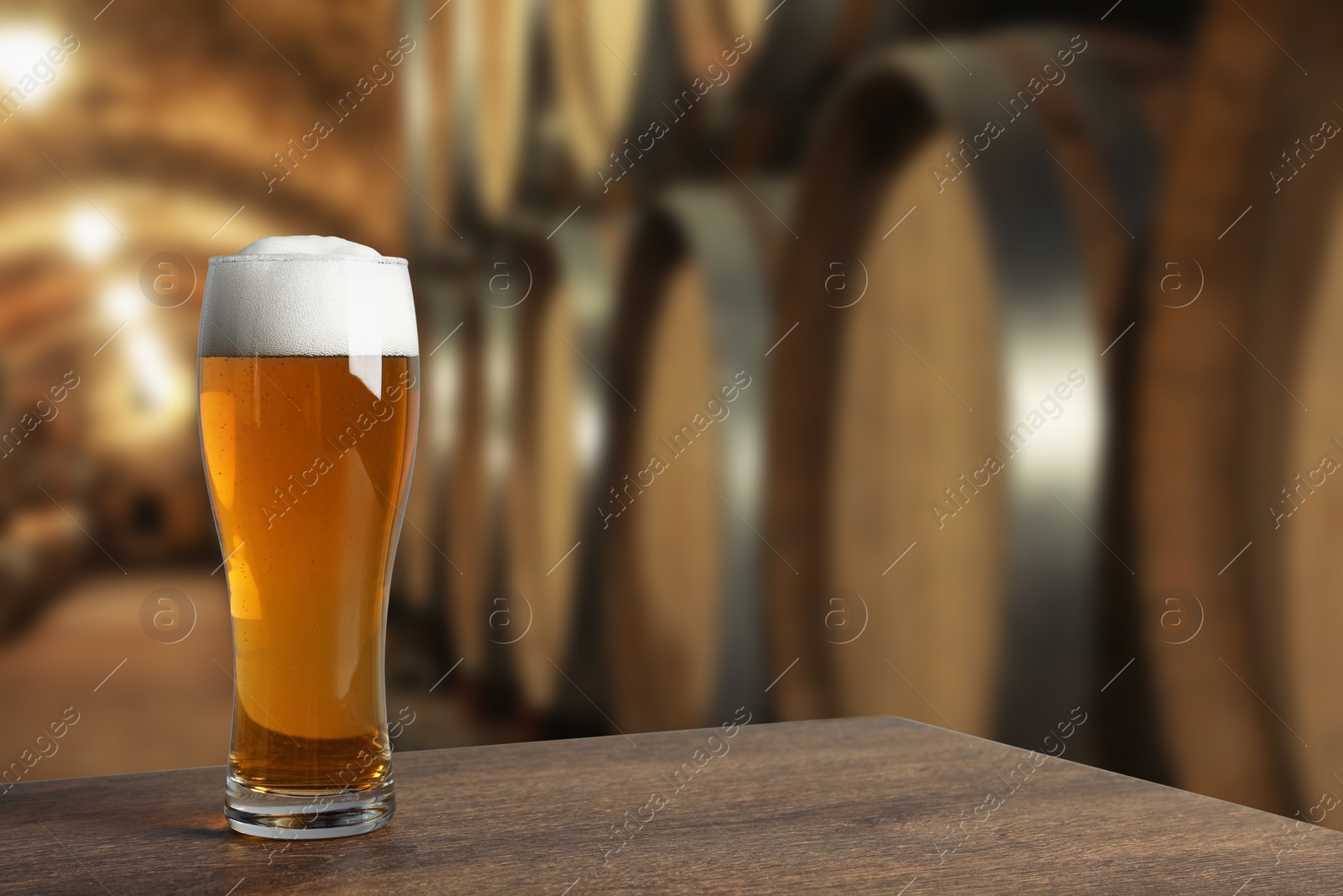 Image of Glass with fresh beer on wooden table in cellar, space for text