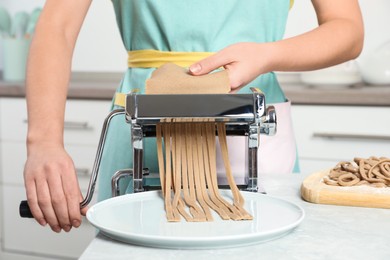 Woman preparing soba (buckwheat noodles) with pasta maker machine in kitchen, closeup