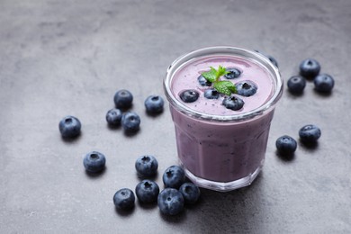 Photo of Glass of blueberry smoothie with mint and fresh berries on grey table. Space for text