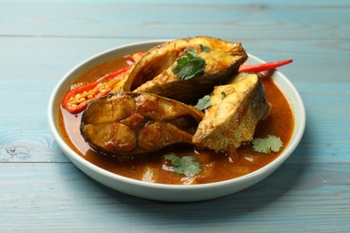Photo of Tasty fish curry on light blue wooden table, closeup. Indian cuisine