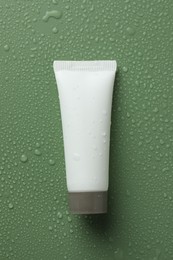 Photo of Moisturizing cream in tube on green background with water drops, top view