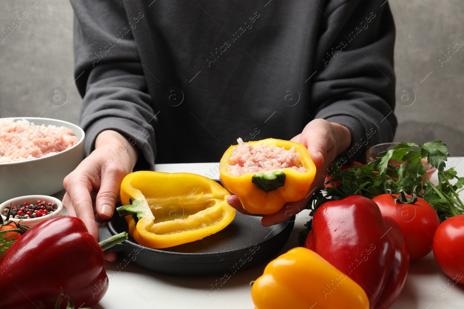 Photo of Woman making stuffed peppers with ground meat at white table, closeup