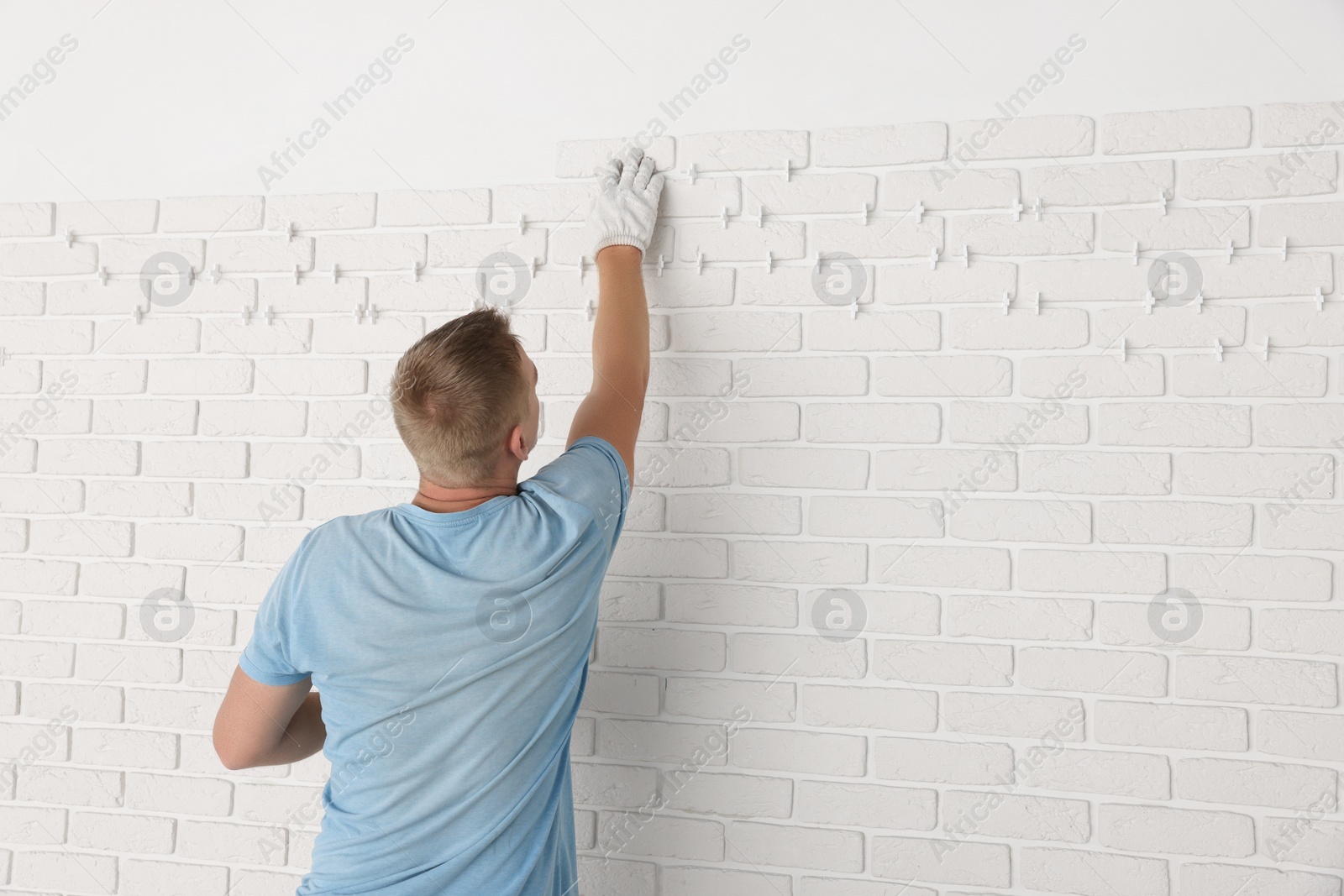 Photo of Professional builder installing new white decorative bricks on wall, back view