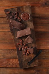 Photo of Pieces of tasty milk chocolate, cocoa beans and powder on wooden table, top view