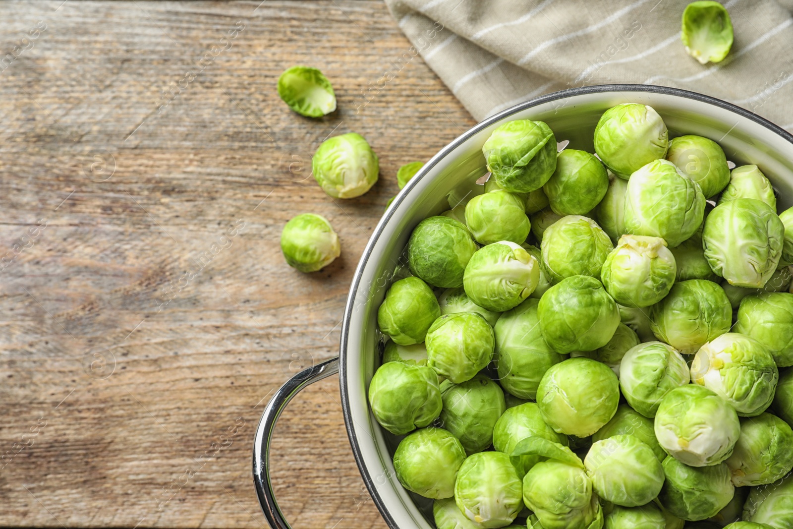 Photo of Colander with Brussels sprouts on wooden background, top view. Space for text