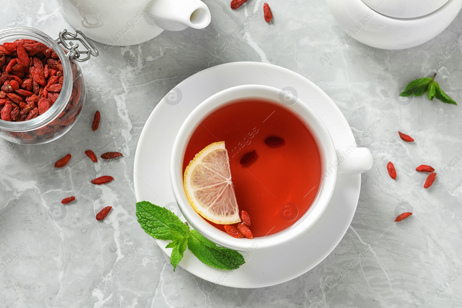 Photo of Cup of healthy goji tea with lemon on grey table, flat lay