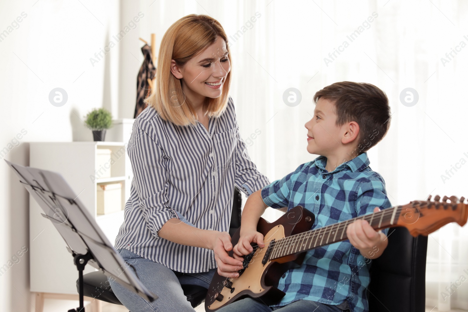 Photo of Little boy playing guitar with his teacher at music lesson. Learning notes