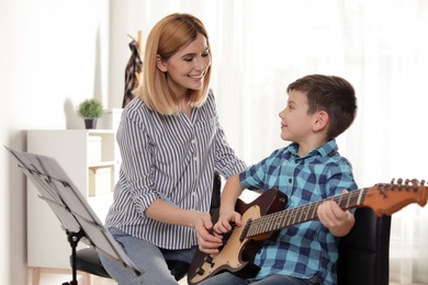 Little boy playing guitar with his teacher at music lesson. Learning notes