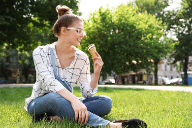 Photo of Young happy woman with ice cream sitting on grass in park. Space for text
