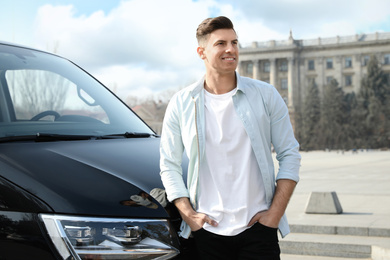 Handsome man near modern car on city street