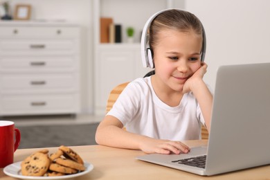 Photo of Little girl in headphones using laptop at table indoors, space for text. Internet addiction