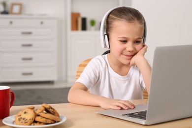 Little girl in headphones using laptop at table indoors, space for text. Internet addiction