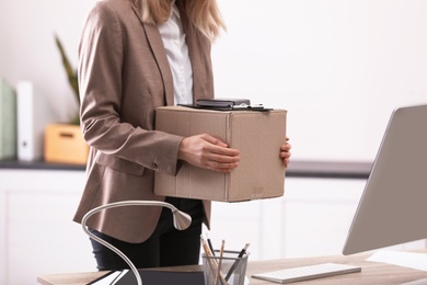 Young woman holding moving box with office stuff indoors, closeup