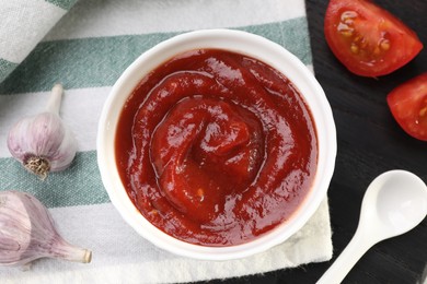 Photo of Organic ketchup in bowl, fresh tomatoes and garlic on table, flat lay. Tomato sauce