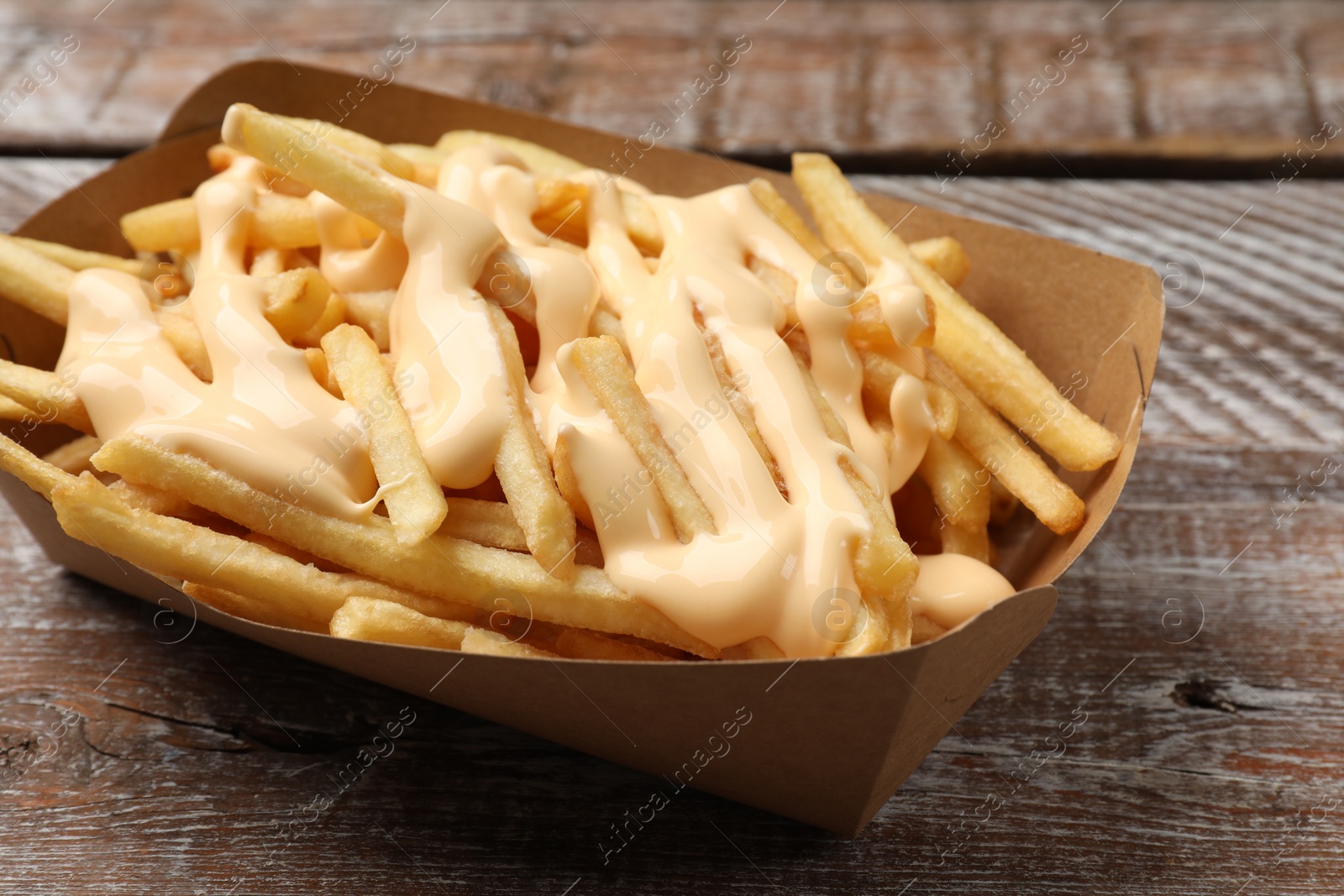 Photo of Delicious French fries with cheese sauce on wooden rustic table, closeup